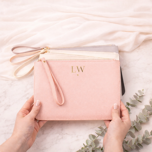 Pink clutch bag with initials held by hands on a light background