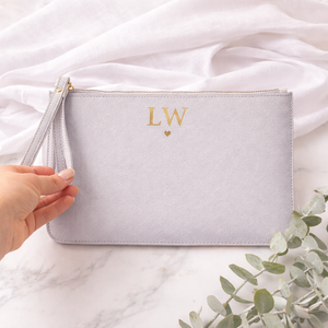Light gray pouch with 'LW' initials held by a hand on a white fabric background