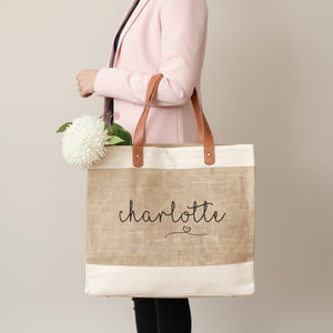 Tote bag with 'Charlotte' printed on it, held by a person with flowers in the background.