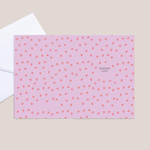 Pink card with red heart pattern and 'Sending Love' text on a beige background