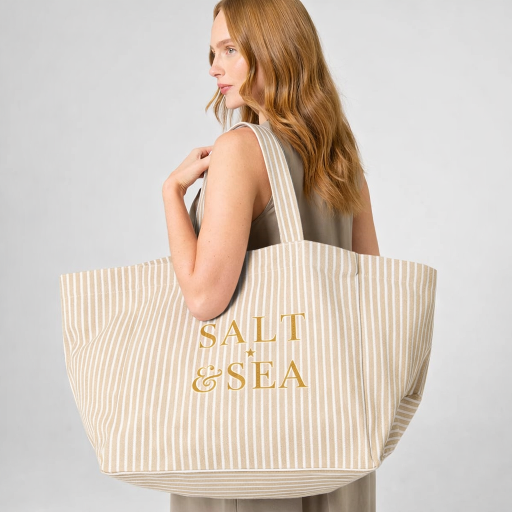 Woman holding a striped tote bag with 'Salt & Sea' text on a plain background