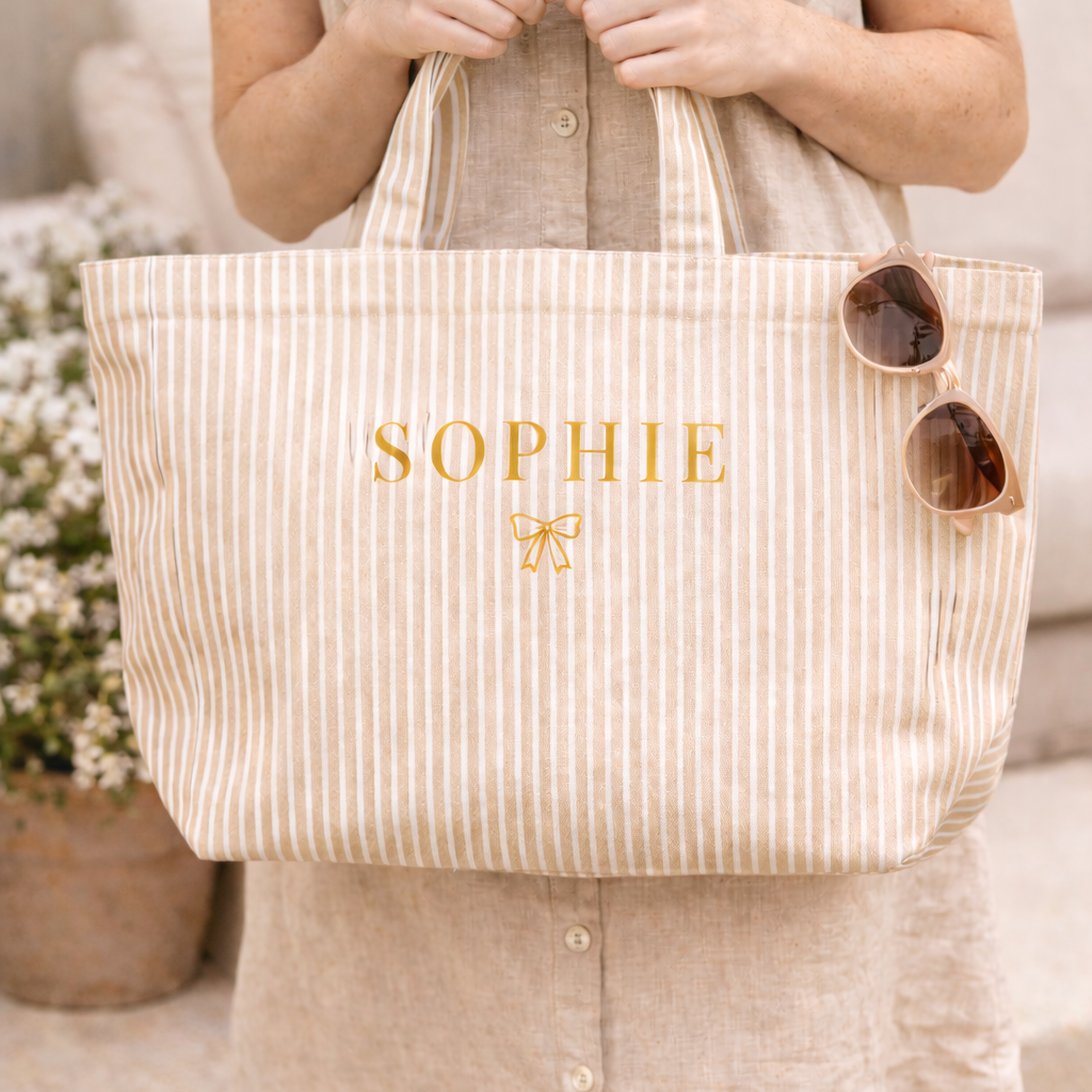 Person holding a striped tote bag with 'SOPHIE' and a butterfly emblem.