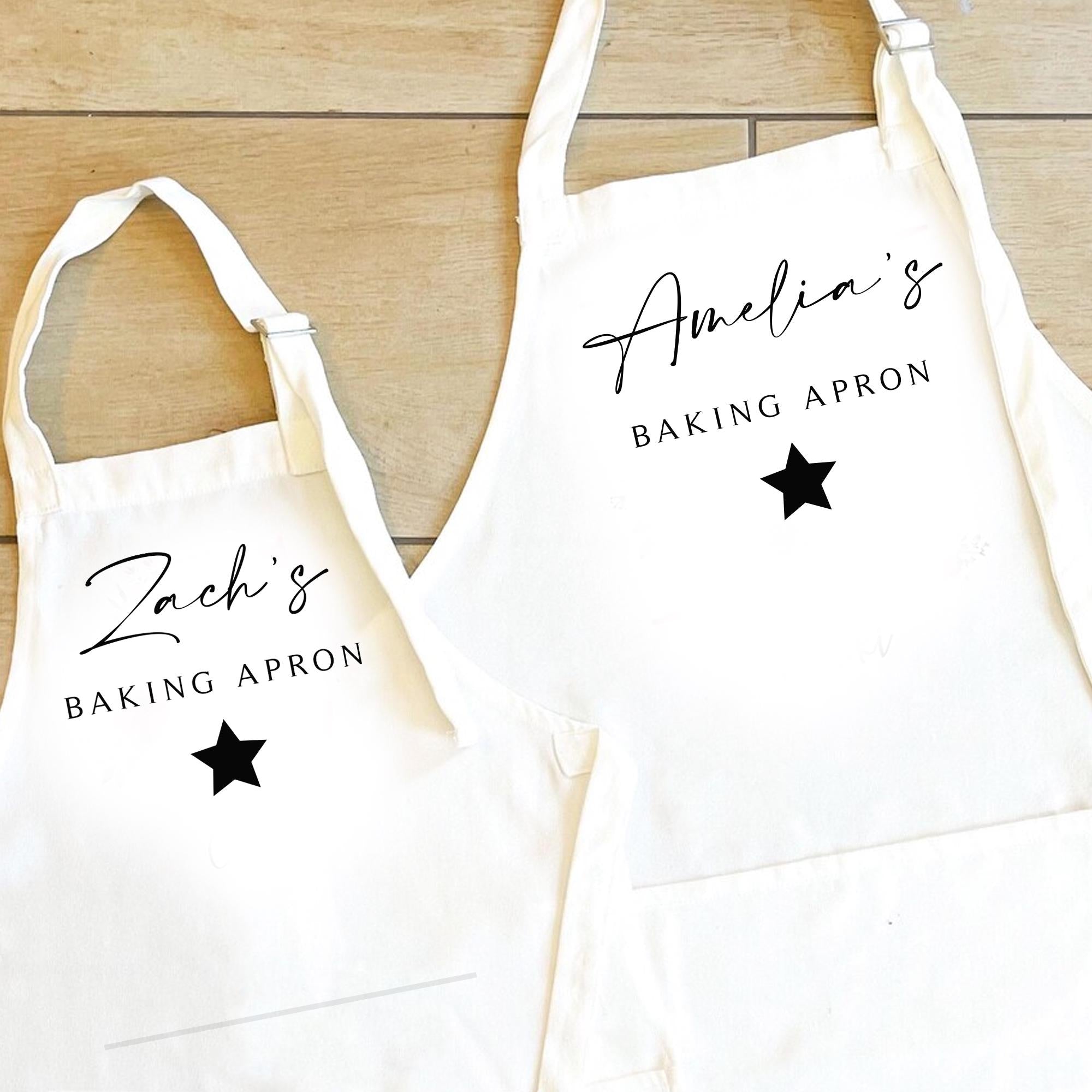 Two white aprons with personalized names and star designs on a wooden surface.