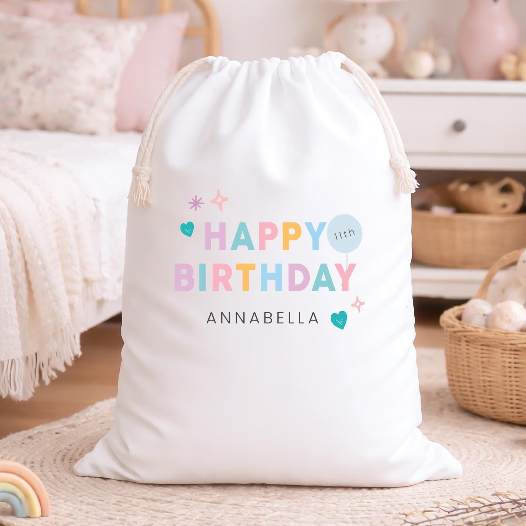 White drawstring bag with 'Happy Birthday Annabella' text in colorful letters on a soft surface.
