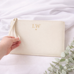 Beige pouch with initials 'LW' held by a hand on a white fabric background