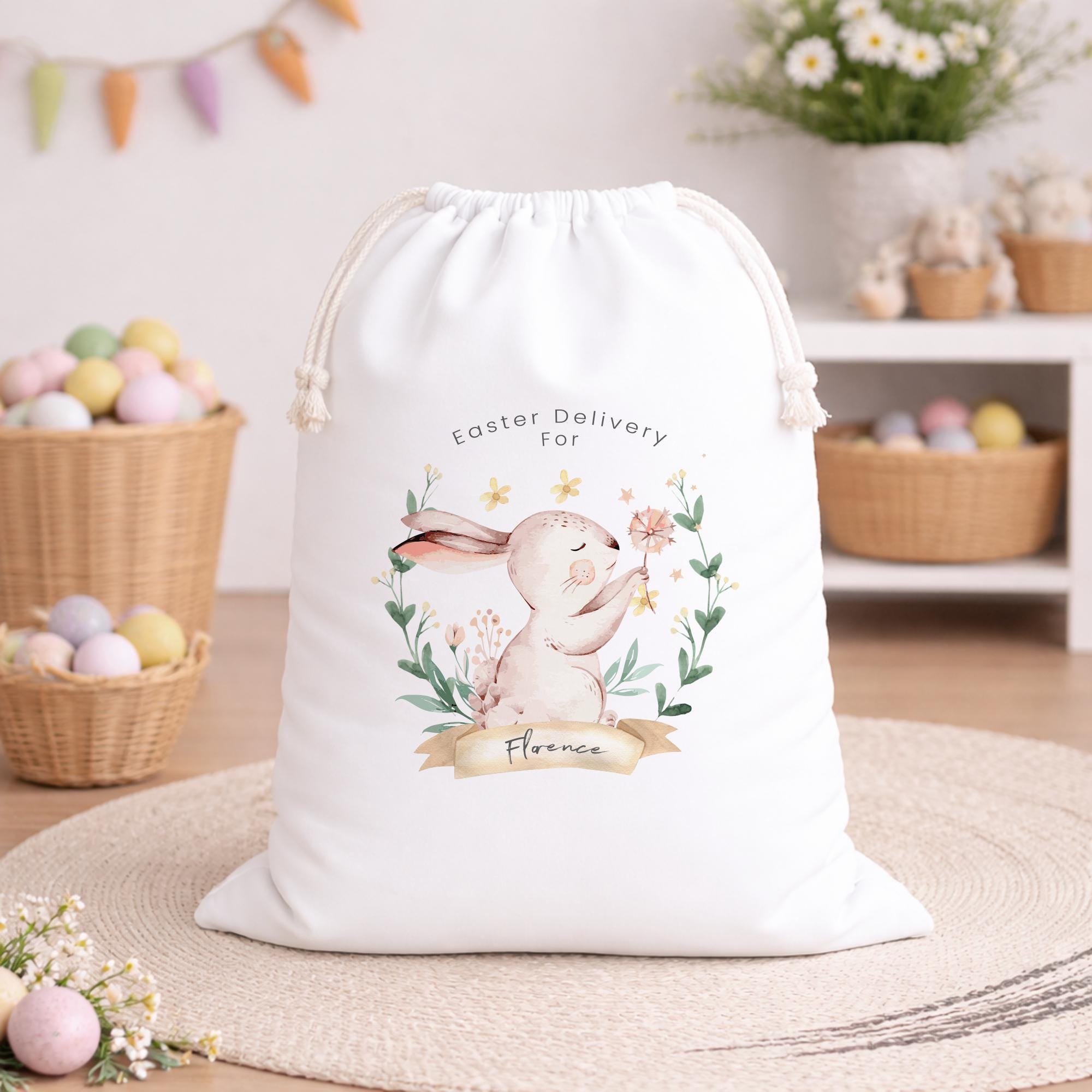 White drawstring bag with Easter design featuring a bunny and flowers, placed on a wooden floor with Easter decorations in the background.