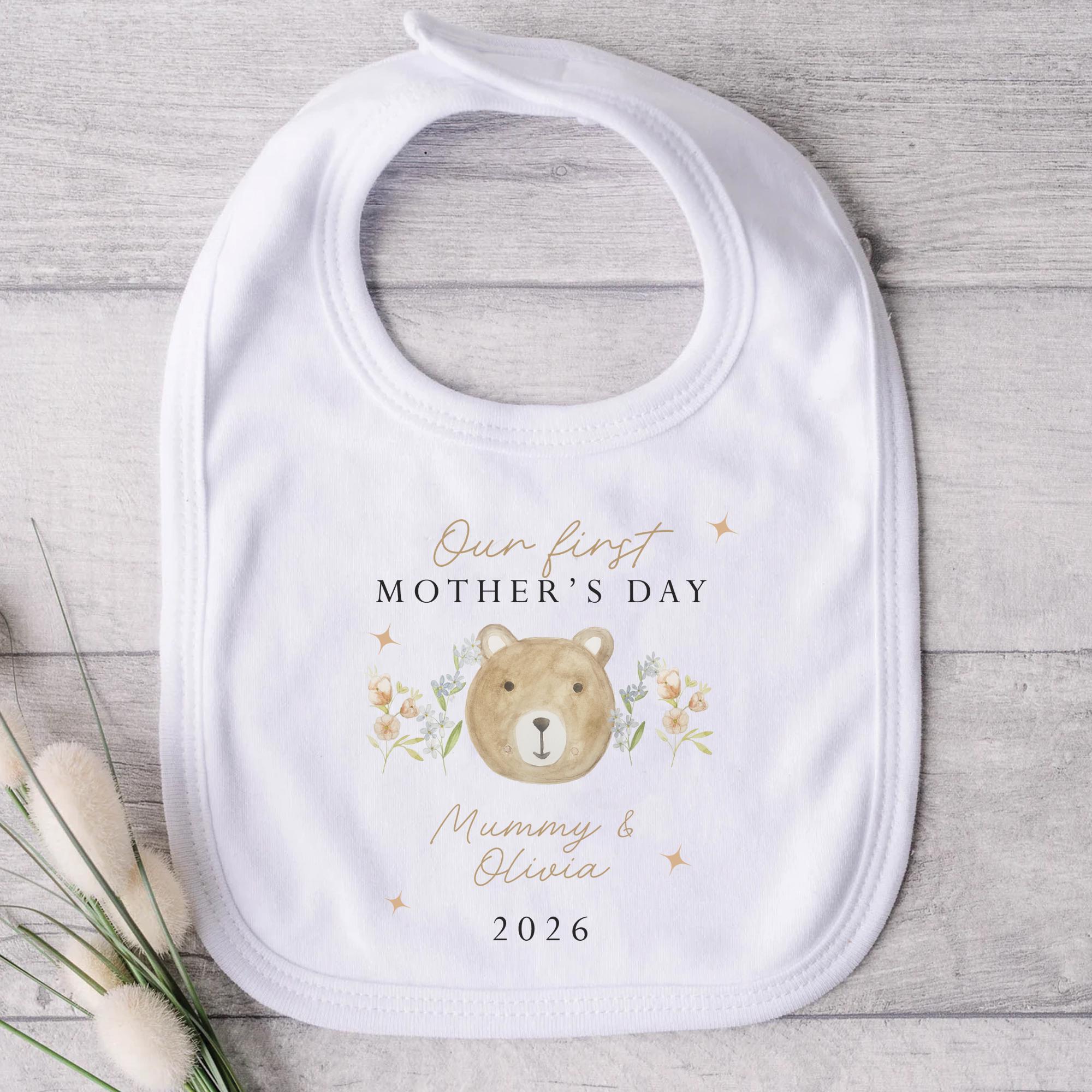 Baby bib with bear illustration and text on a wooden surface