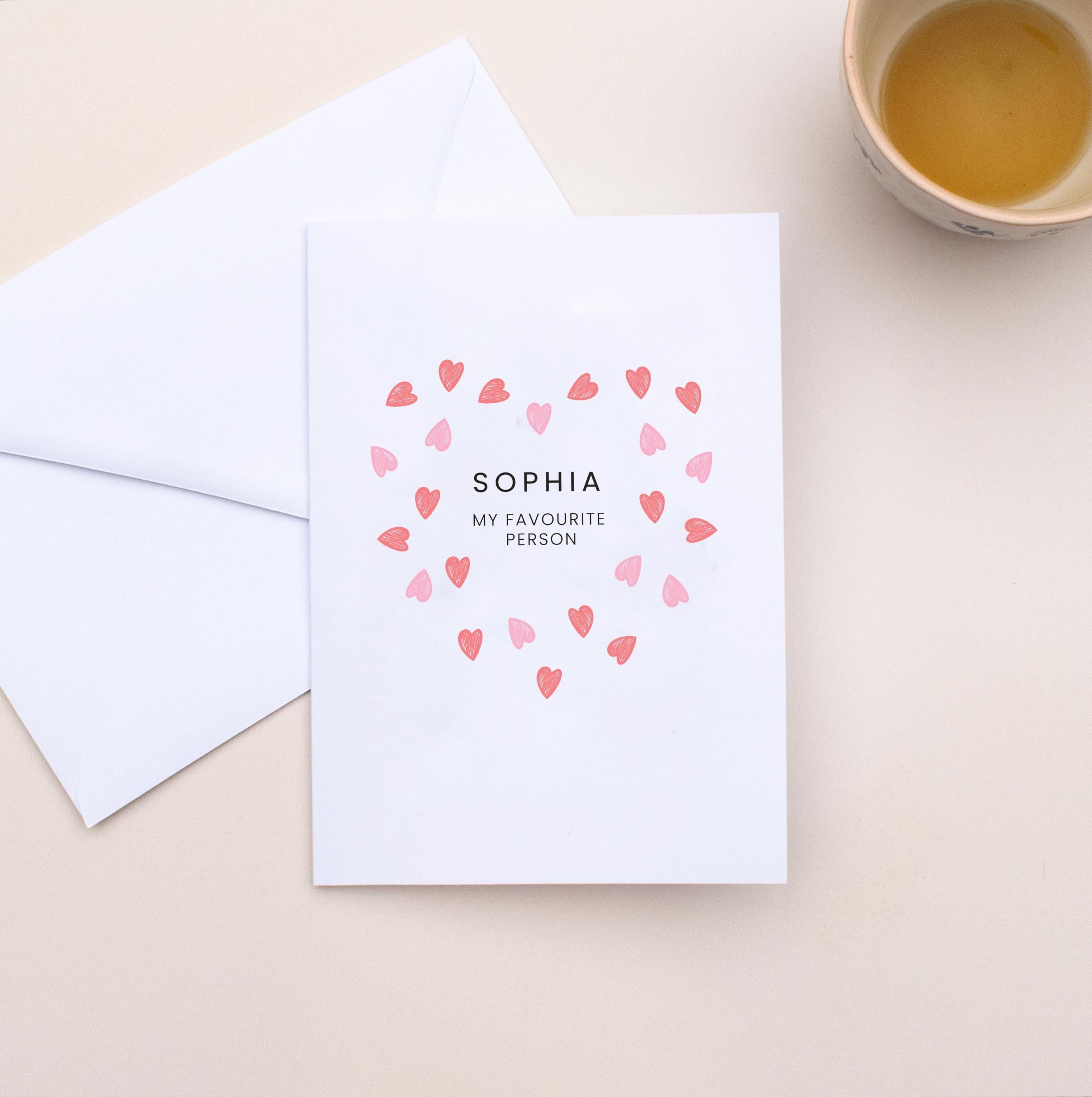 Greeting card with heart design and text on a beige surface with an envelope and cup of tea.