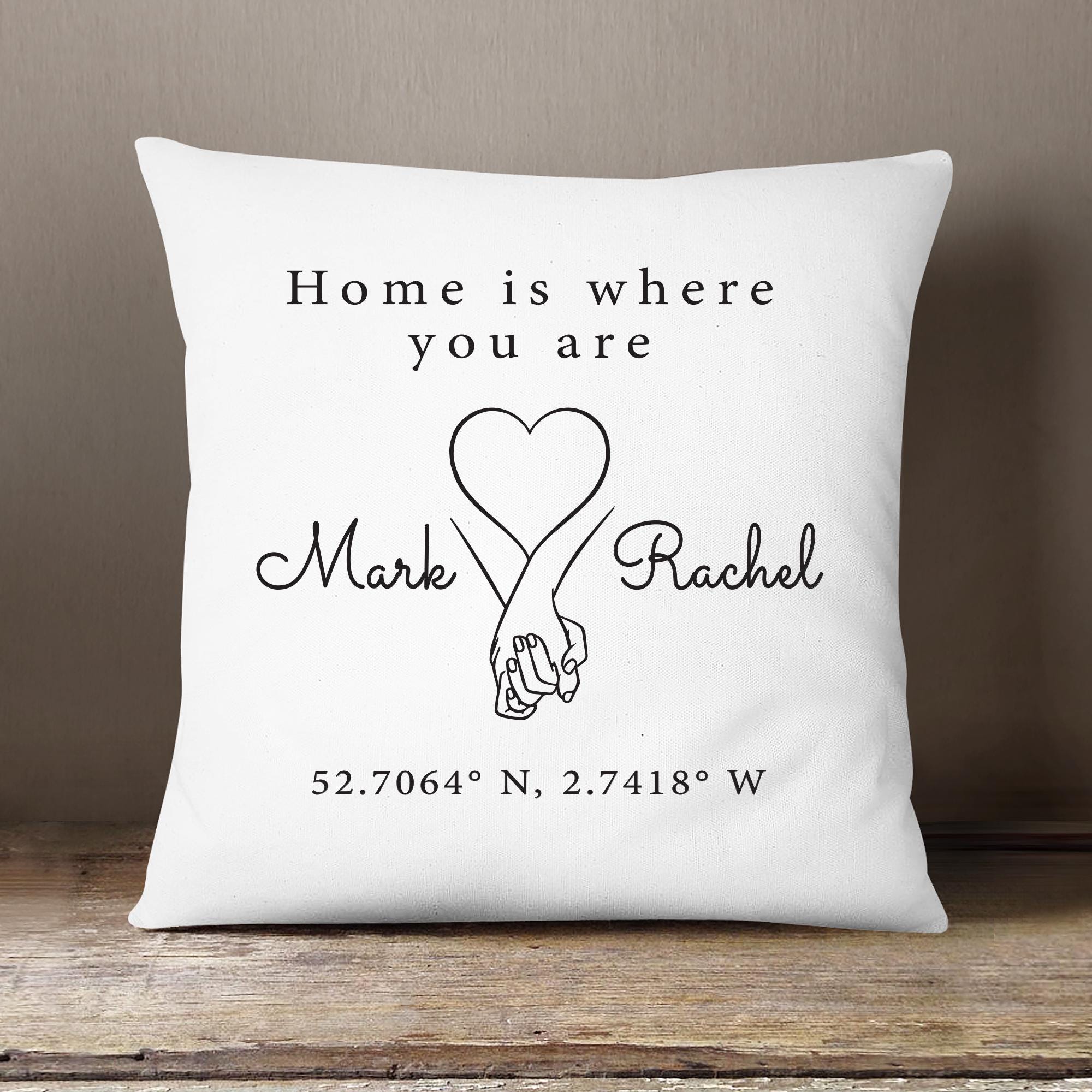 White pillow with black text and a heart design on a wooden surface.