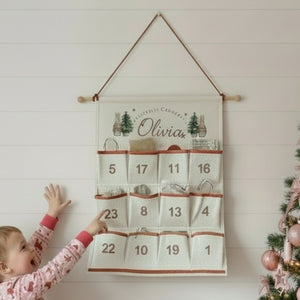 Child reaching towards a Christmas-themed advent calendar hanging on a wall.