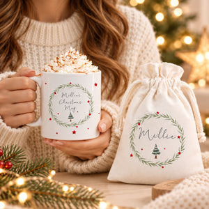 Person holding personalised Christmas wreath mug beside matching Millie hot chocolate gift bag