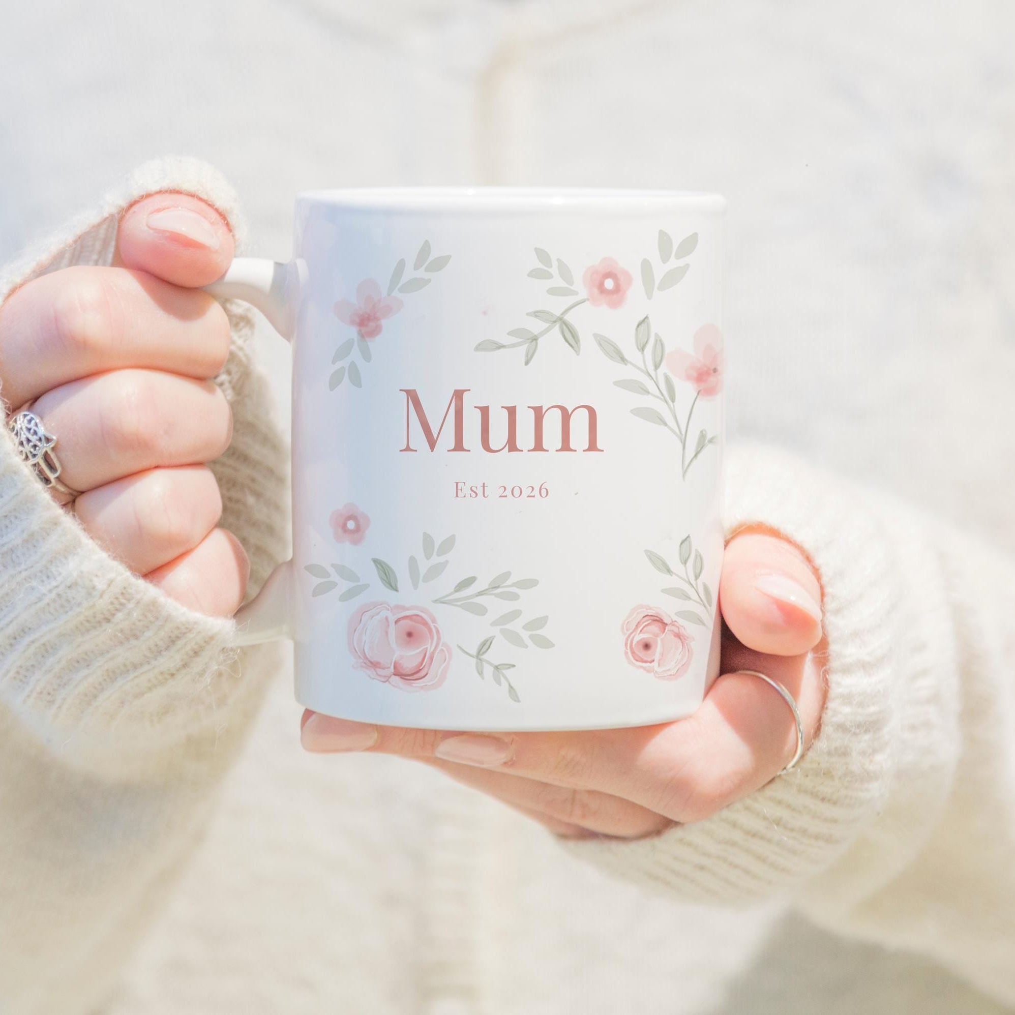 Person holding a mug with 'Mum' printed on it, wearing a white sweater.