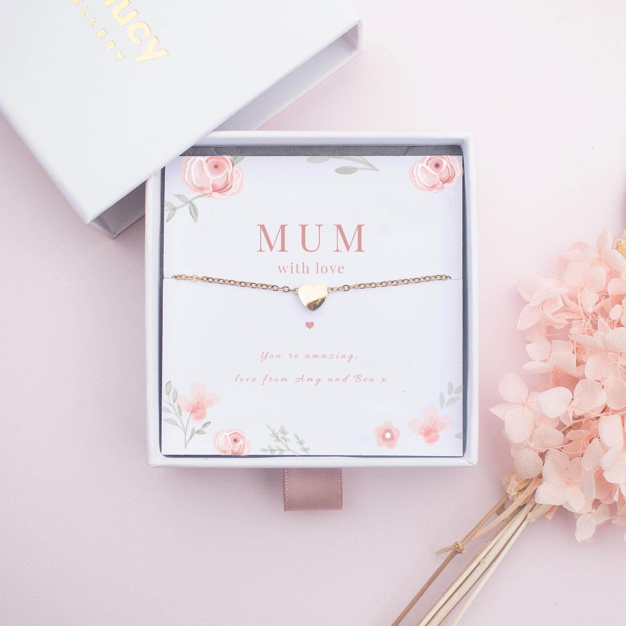 Necklace with a heart pendant on a floral card labeled 'MUM with love' on a pink background.