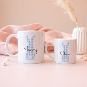 Two white mugs with blue bunny designs and names 'Mummy' and 'Olivia' on a pink background.
