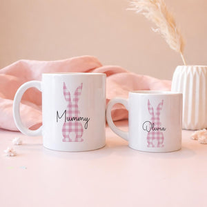 Two white mugs with pink bunny designs and names on a soft pink background