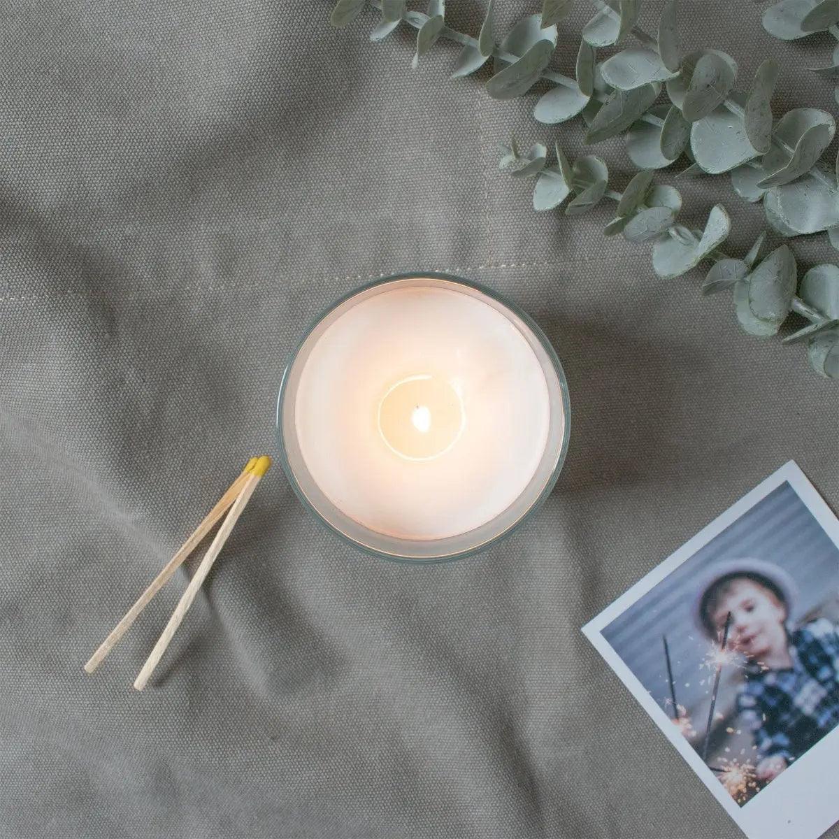 Overhead view of a lit personalised candle with matches and a photograph