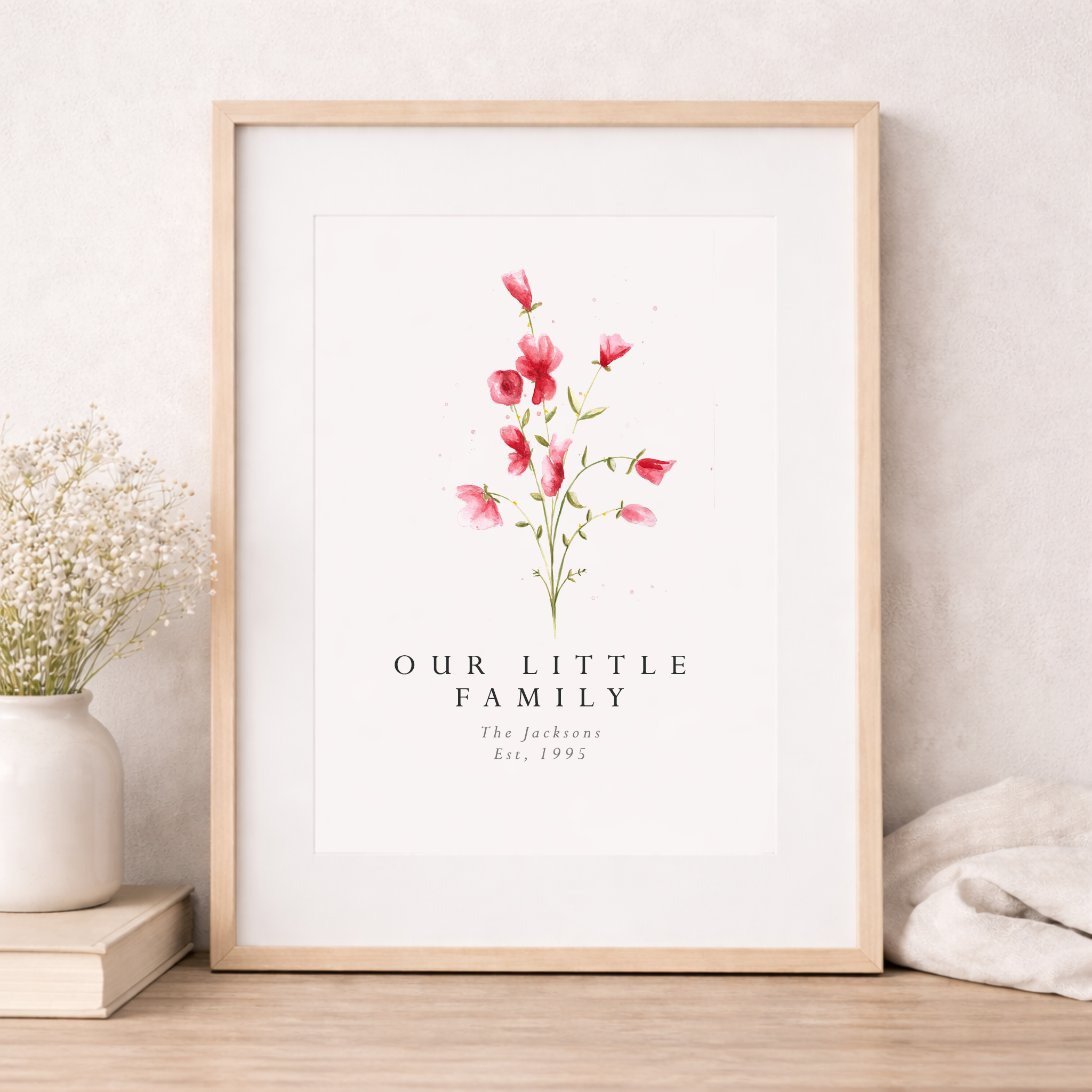 Framed artwork with floral design and text 'Our Little Family' on a white wall.