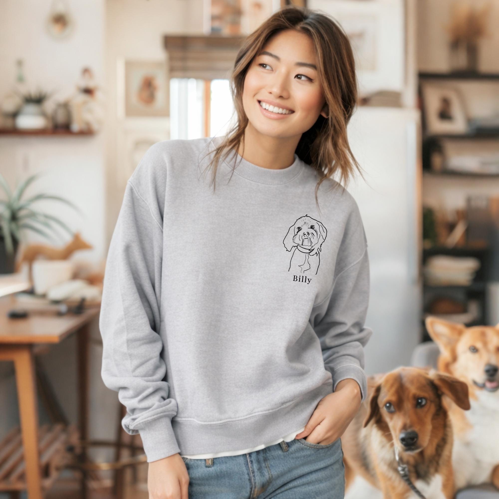 Woman wearing a gray sweatshirt with a dog illustration and name, standing in a home setting with two dogs.