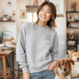 Woman wearing a gray sweatshirt with a dog illustration and name, standing in a home setting with two dogs.