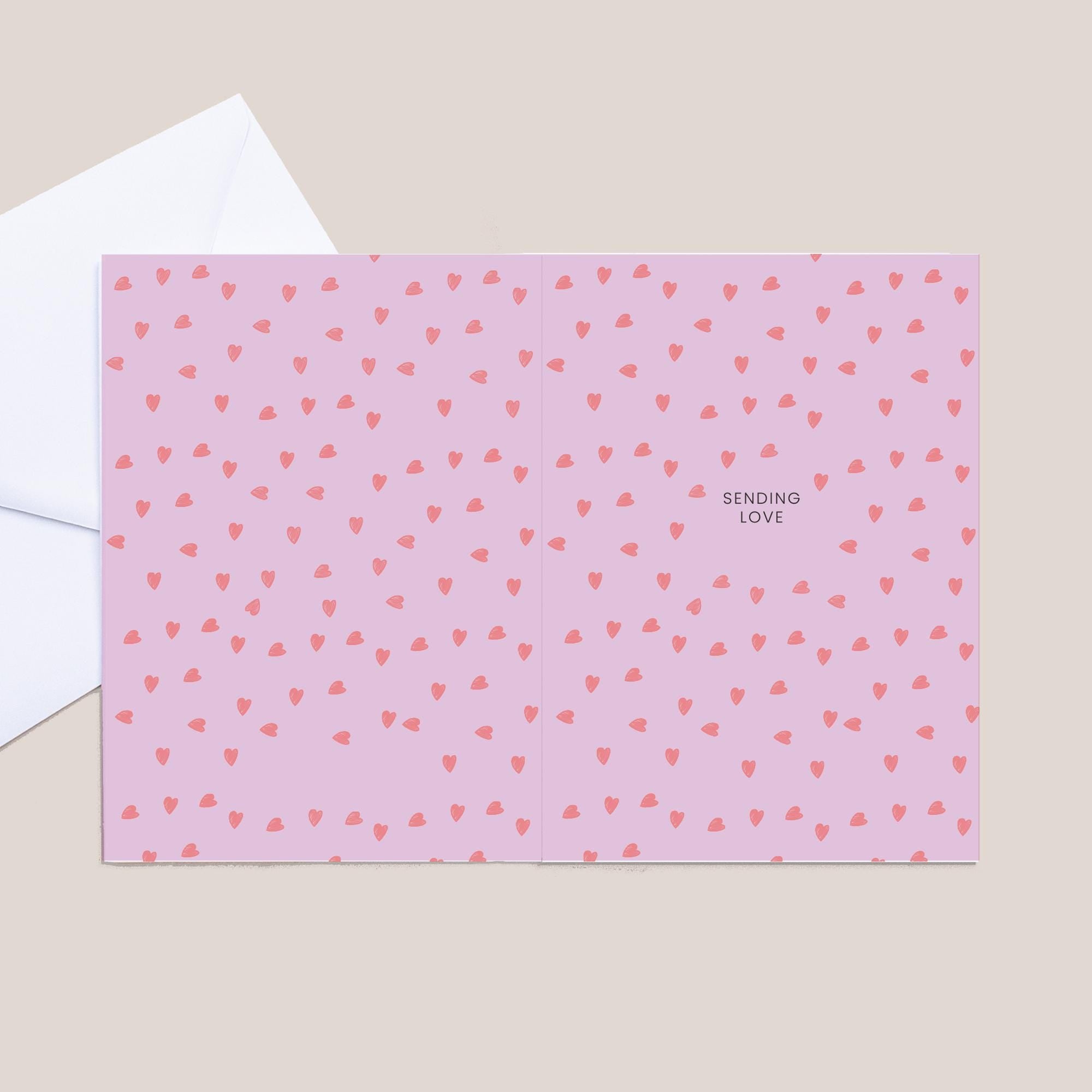 Pink card with red heart pattern and 'Sending Love' text on a beige background