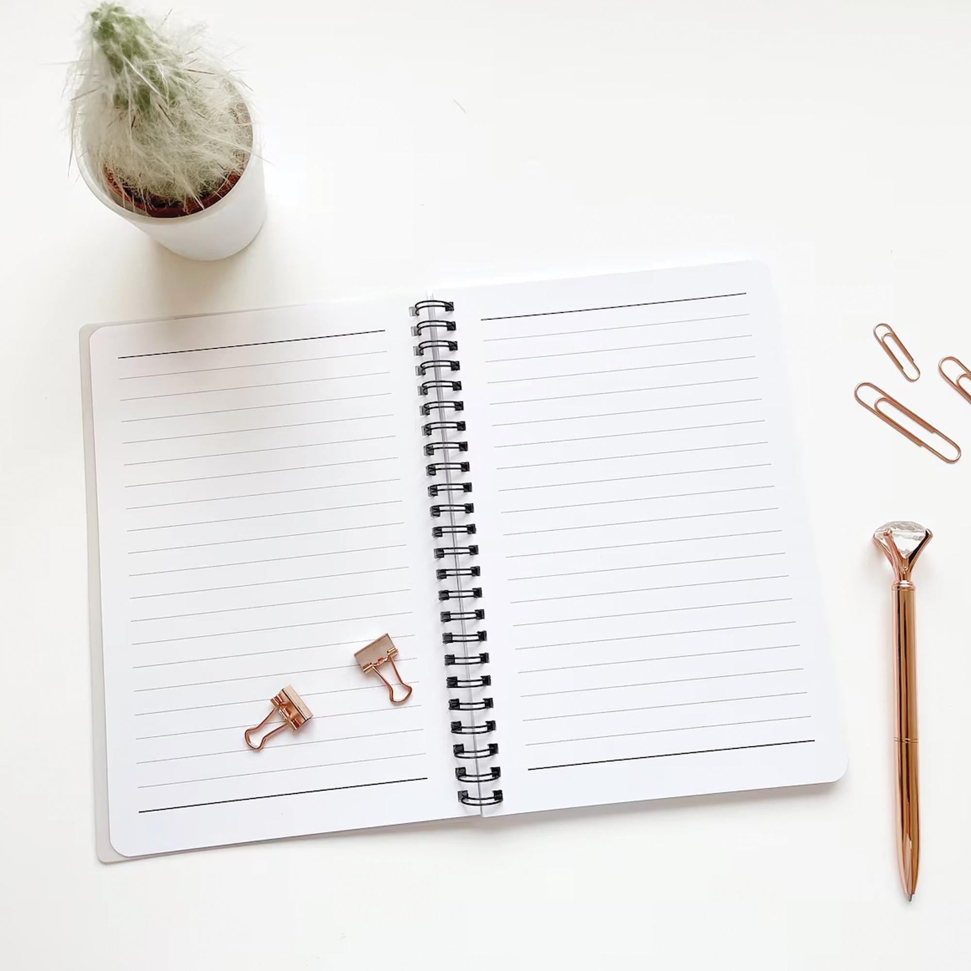 Open notebook with rose gold clips and pen on a white surface