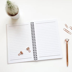 Open notebook with rose gold clips and pen on a white surface